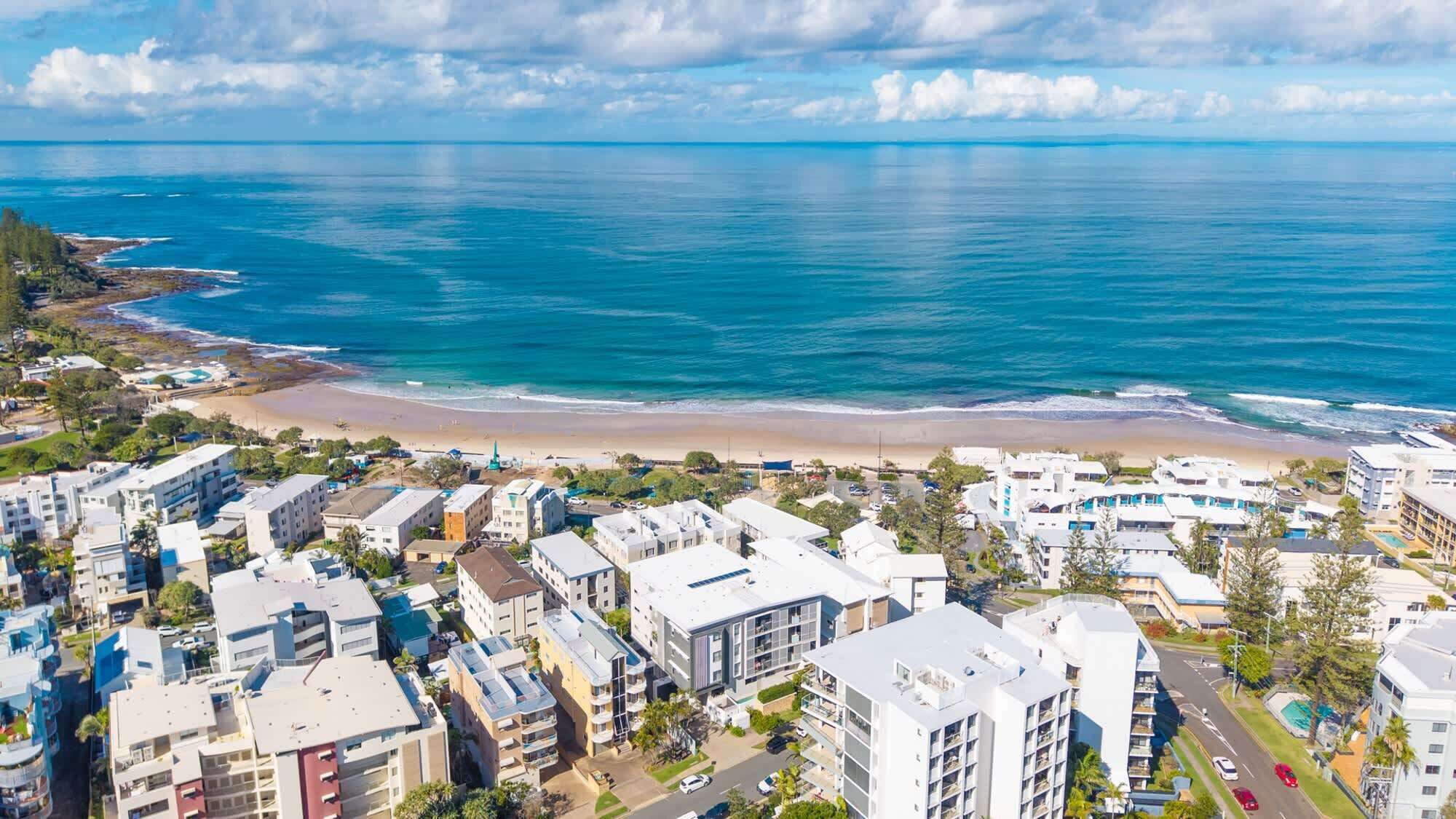 Una zona residencial costera con propiedades frente a la playa, incluyendo edificios de varios pisos y una playa al fondo.