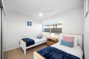 Ein Schlafzimmer mit zwei Betten, einem Deckenventilator, einem Fenster mit Blick und einem Nachttisch mit Lampe.