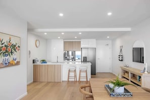 A modern kitchen with a central island, wooden cabinets, and a stainless steel refrigerator. - Beachside 3-bed apartment with Ocean Views (Kings Beach)