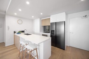 A modern kitchen with white cabinetry, a stainless steel refrigerator, a built-in oven, and a white island with bar stools.