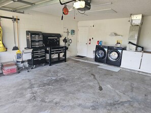 Een garage met een werkbank, een wasmachine en een bezem.