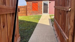 Ein Holzzaun, ein Betonweg und ein rotes Gebäude mit einer Tür.
