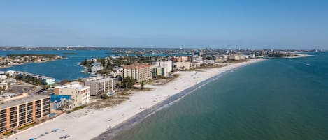 Vista aérea de una ciudad costera con una extensa playa arenosa, varios edificios de múltiples pisos y un puerto deportivo.