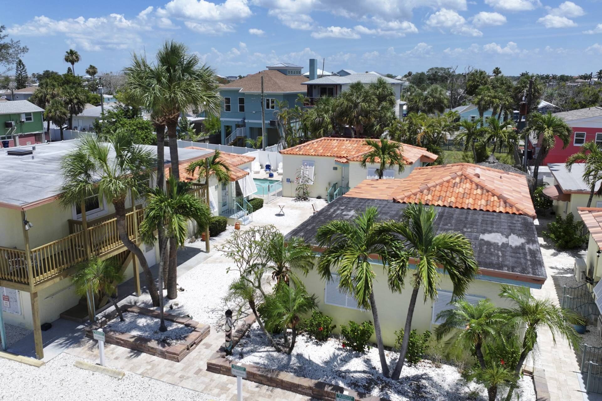 A residential area with multiple houses, some with tiled roofs and others with flat roofs, surrounded by palm trees.