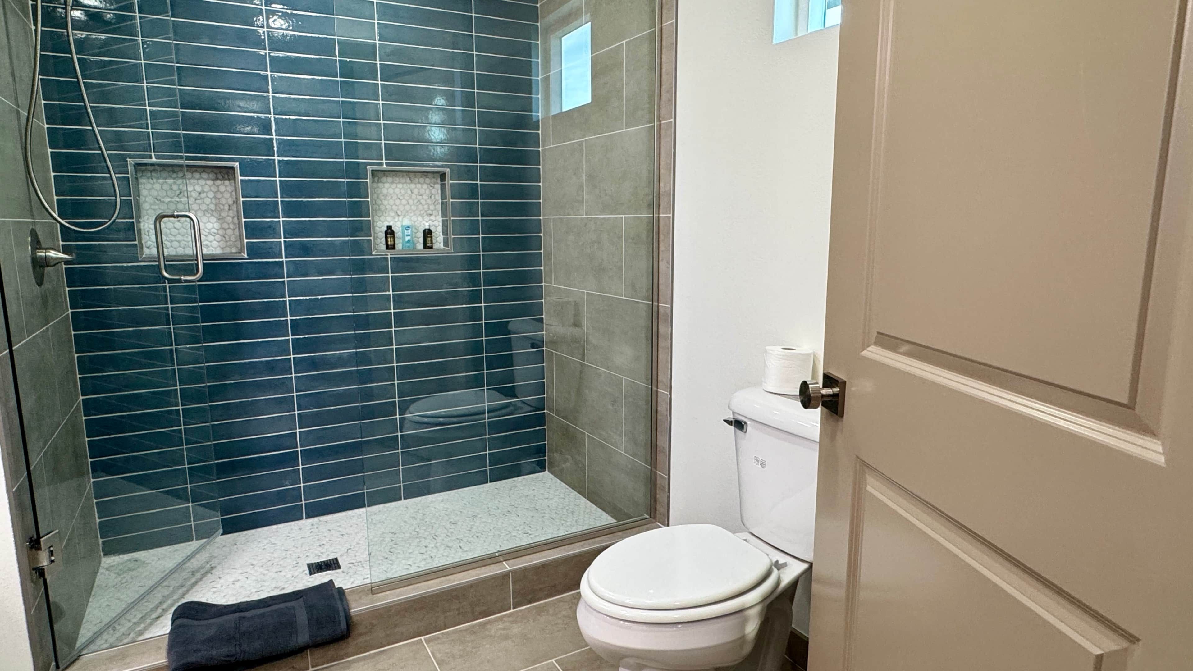 A bathroom with a glass shower enclosure, a white toilet, and a towel on the floor.