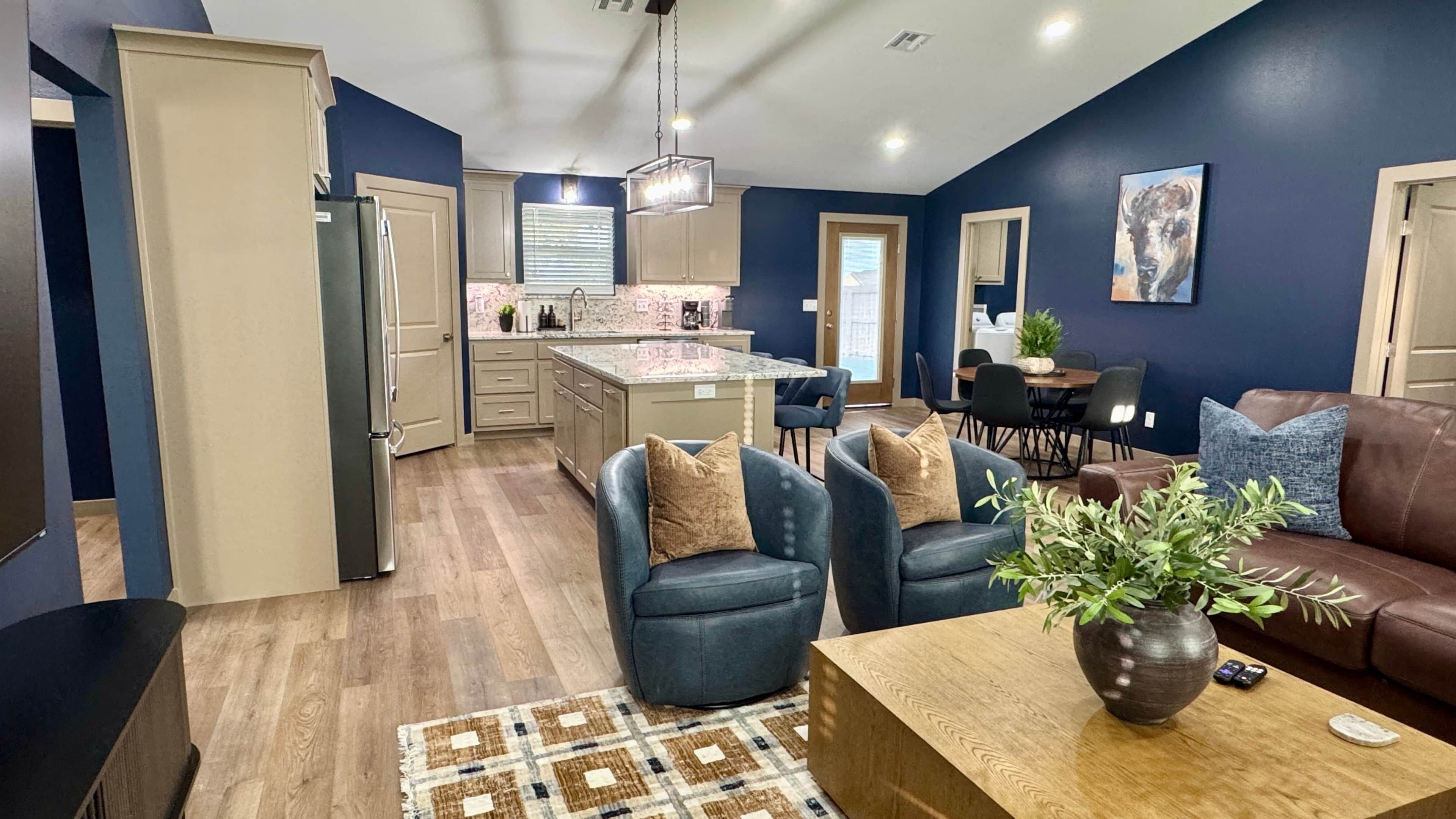 A modern kitchen with a central island, a dining area with a table and chairs, and a living room with a sofa and a coffee table.