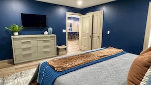 A bedroom with a bed, dresser, TV, and a hallway leading to a dining area. - Guy’s Night Out - WinStar Bachelor - King Bed (Thackerville)
