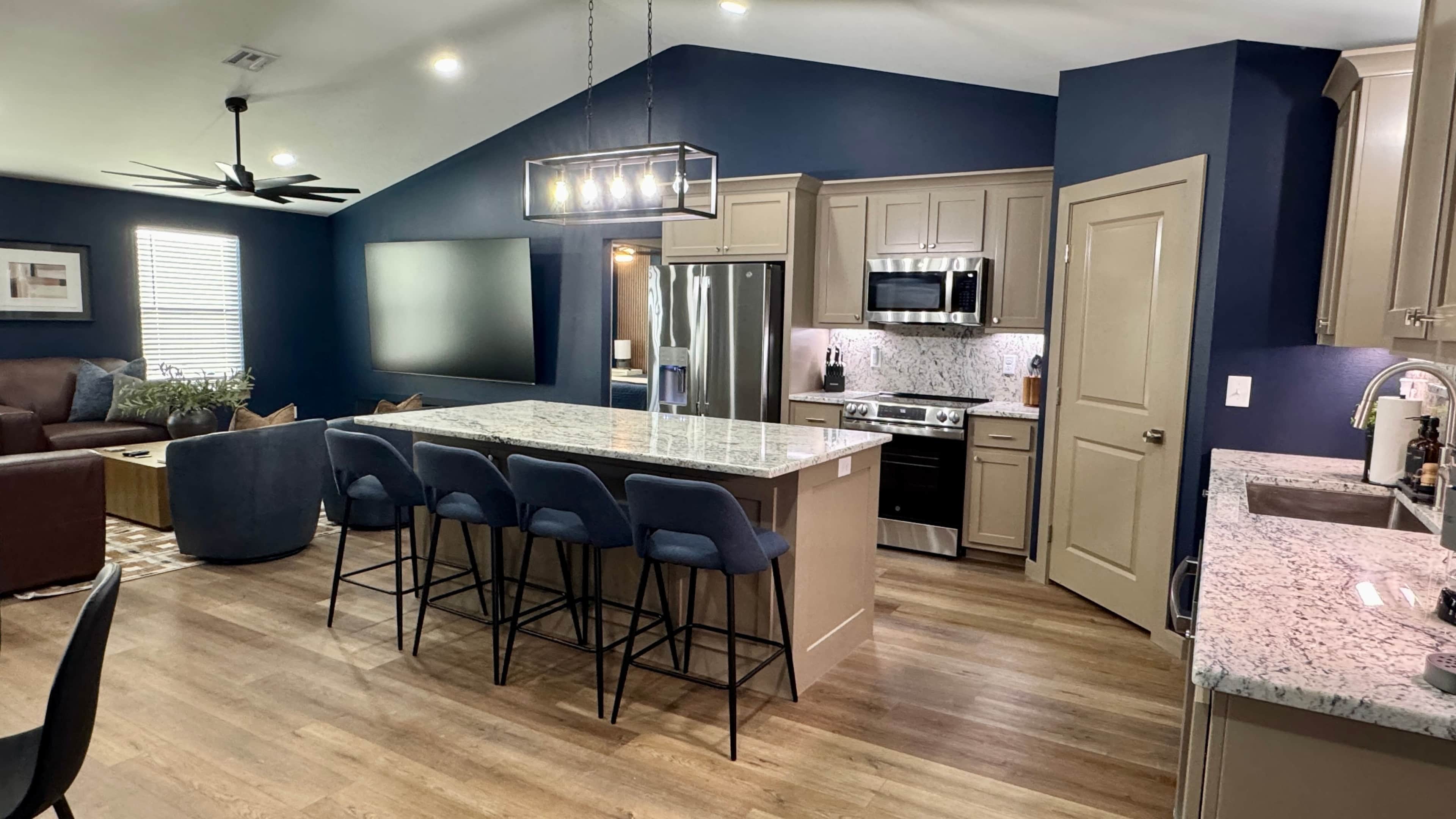 A modern kitchen with a central island, bar stools, a microwave, stove, and a refrigerator.