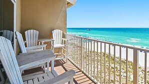 A balcony with white Adirondack chairs and a view of the beach. - Emerald Dunes 502•Updated•Beachfront•Pool +Hot Tub•Beach Gear•Nearby Dining (Destin)