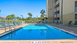 A swimming pool with a 5 1/2 ft depth marker, surrounded by lounge chairs and palm trees. - Emerald Dunes 502•Updated•Beachfront•Pool +Hot Tub•Beach Gear•Nearby Dining (Destin)