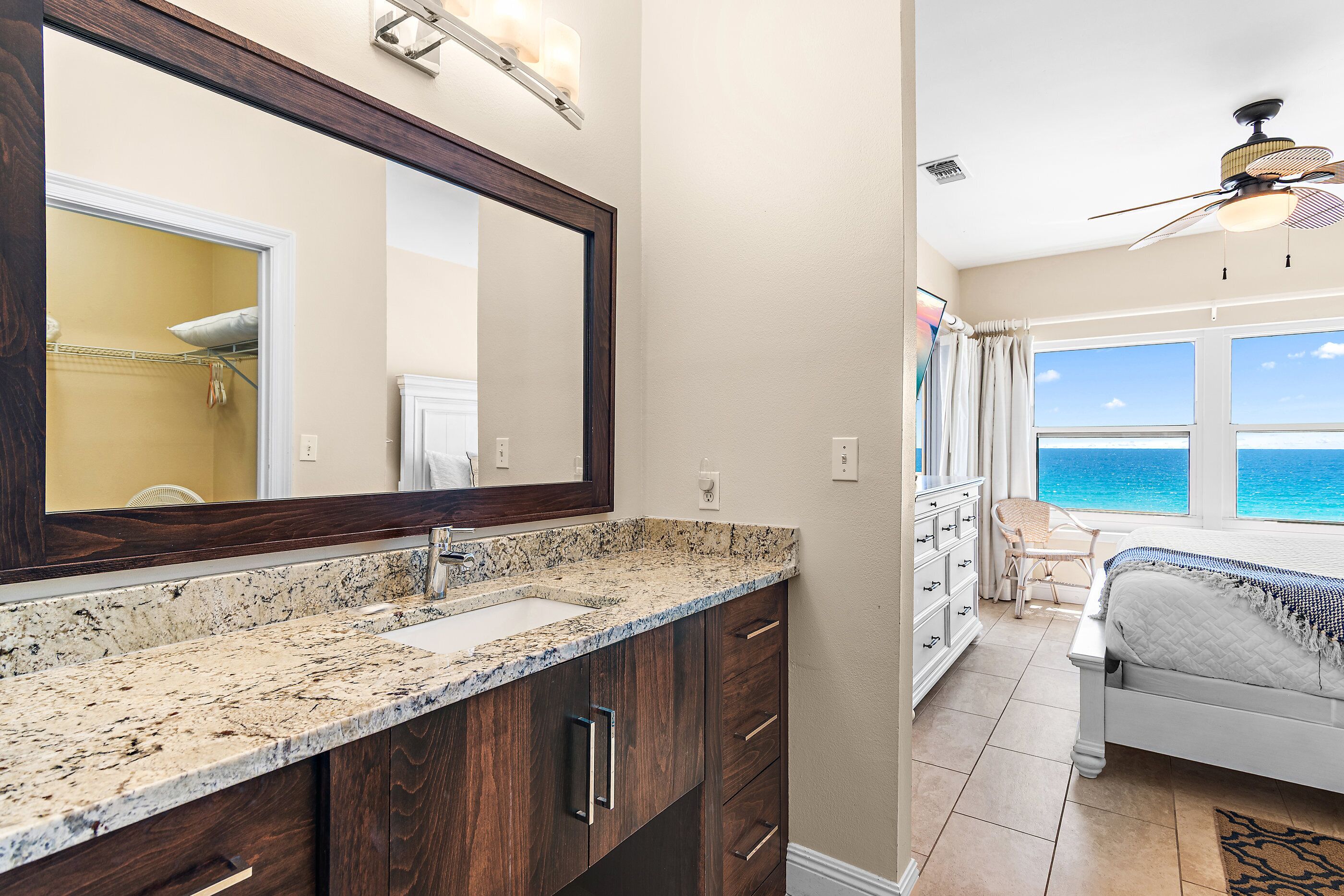 A bathroom with a large mirror, granite countertop, and a view of the ocean through the window.