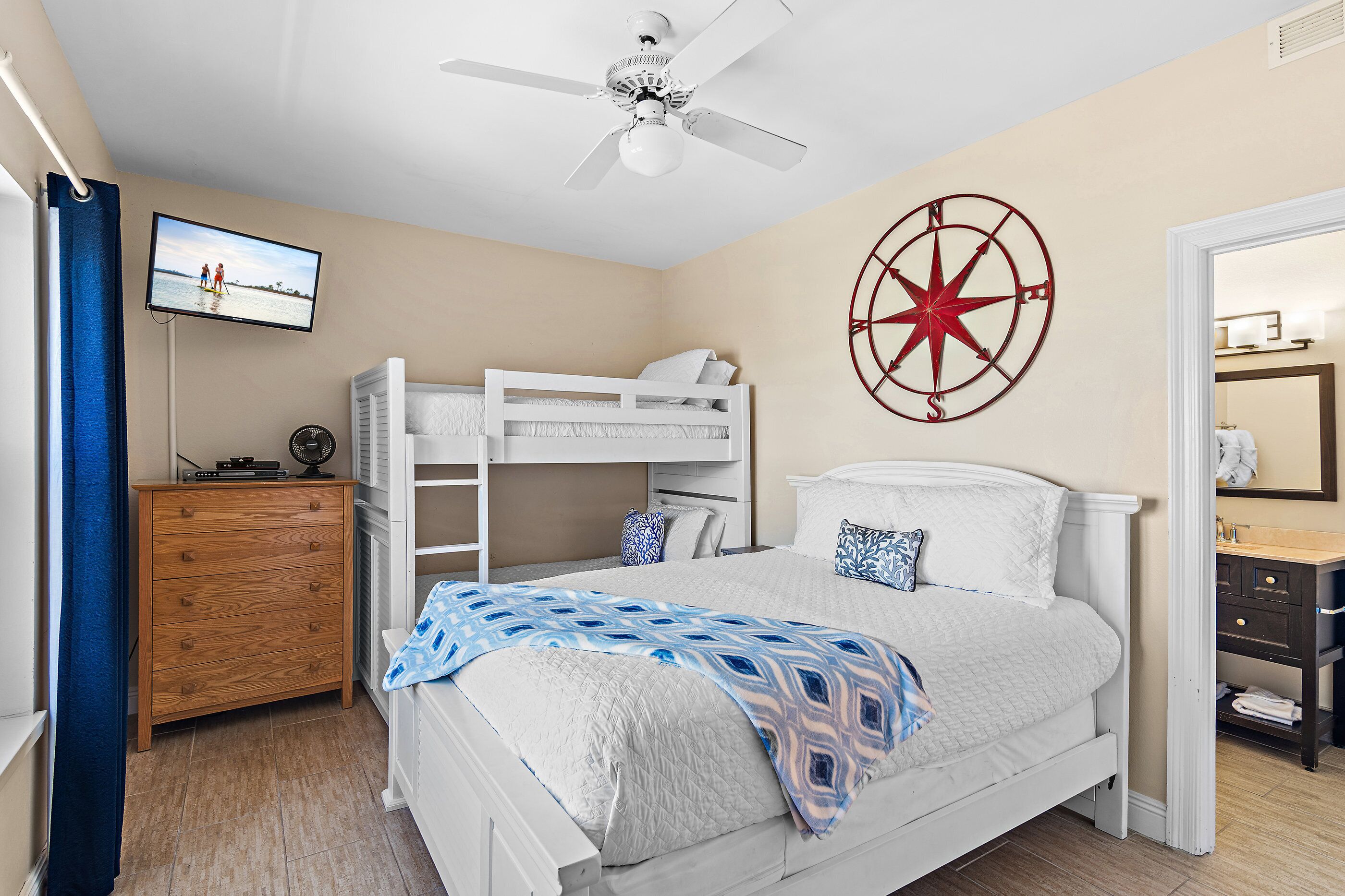 A bedroom with a bunk bed, a ceiling fan, a wall clock, a television, and a bathroom with a mirror and sink.
