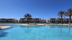 A large outdoor swimming pool with a clear blue water, surrounded by a tiled deck and palm trees. - Beachfront apartment with a terrace and ocean view (Marina Saidia)