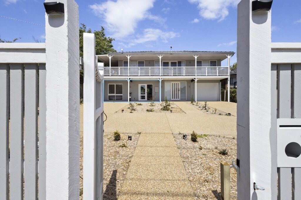 A two-story building with a balcony, a gated entrance, and a gravel driveway.