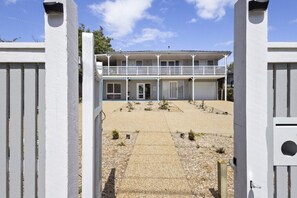 A two-story building with a balcony, a gated entrance, and a gravel driveway. - The Sandman (McCrae)