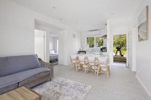 A modern living space with a sofa, dining table, chairs, and a kitchen area. - The Sandman (McCrae)