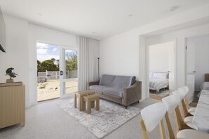 A modern living room with a sofa, a small table, and a dining area with chairs. - The Sandman (McCrae)