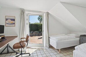 Un dormitori amb un llit, un escriptori amb un ordinador, una cadira i una finestra amb cortines.