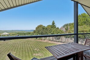 A wooden deck with a table and chairs, overlooking a well-maintained lawn and a distant view of a body of water and trees.