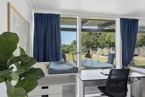 A room with a desk, a chair, a window with curtains, and a view of the outdoors.