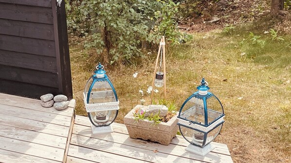 Two lanterns on a wooden deck with a stone planter and a small garden.