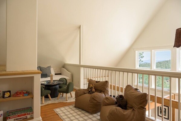 A loft-style room with a high ceiling, a balcony with a railing, a sofa set, and a small table with board games.