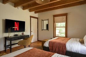 A bedroom with two beds, a desk, a TV, and a window.