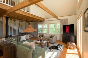 A cozy living room with a sofa, armchairs, a coffee table, a TV, and a dog.