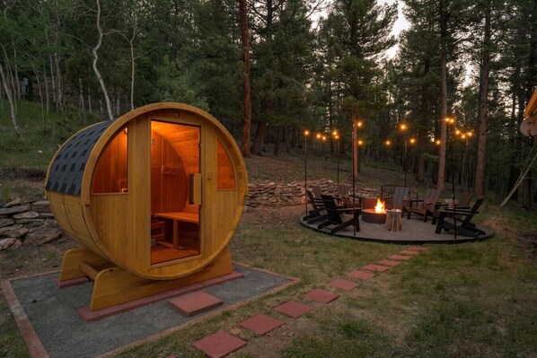 A wooden barrel-shaped cabin with a fire pit and seating area.