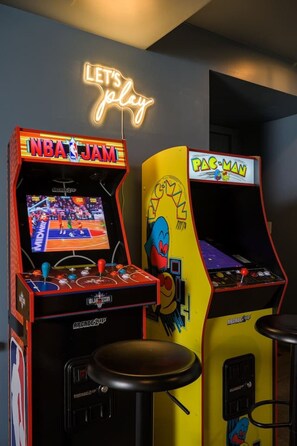 Two arcade machines, one for NBA JAM and another for Pac-Man, with a neon sign above them. - Luxe A-Frame | Hot Tub, Sauna & Stargazing Net (Bailey)
