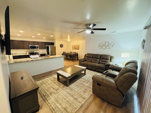 A modern living room with a sofa, coffee table, and a dining area in the background.
