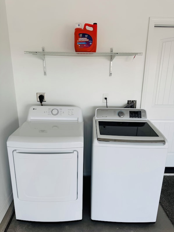 Two white front-loading washing machines side by side, a red detergent bottle on a shelf above, and a door in the background.