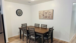 Ein Essbereich mit Holztisch und -stühlen, einer Wanduhr und einem floralen Kunstwerk.