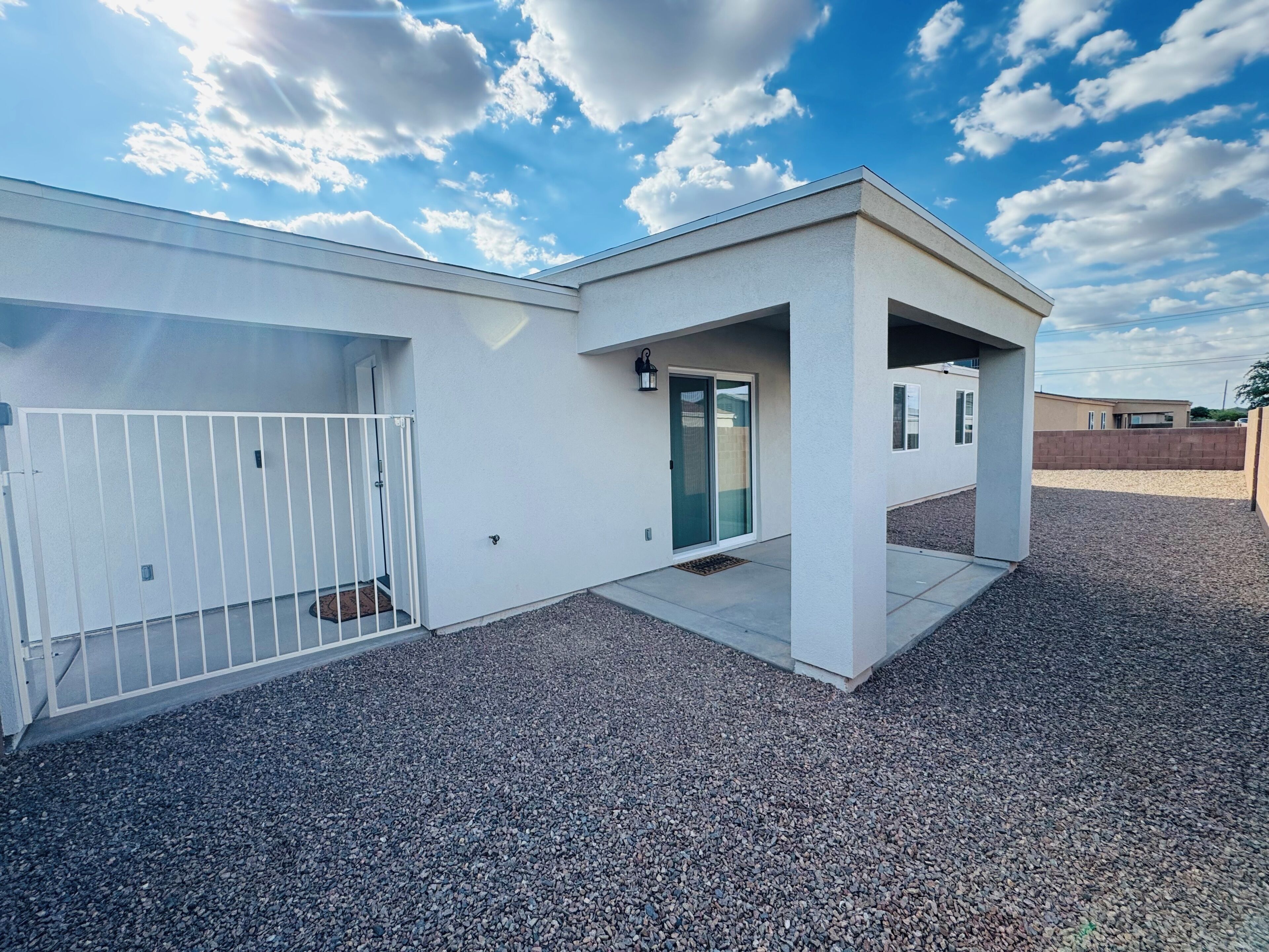 A modern building with a white exterior, a gated entrance, and a gravel driveway.