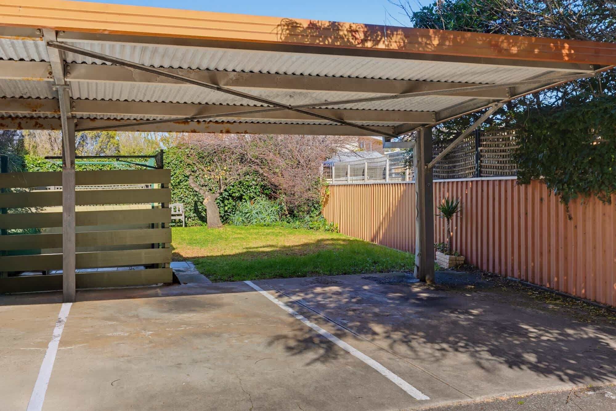 A covered outdoor area with a concrete floor, a wooden bench, and a metal fence.