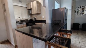 A modern kitchen with a central island, wooden cabinets, a refrigerator, and a microwave.