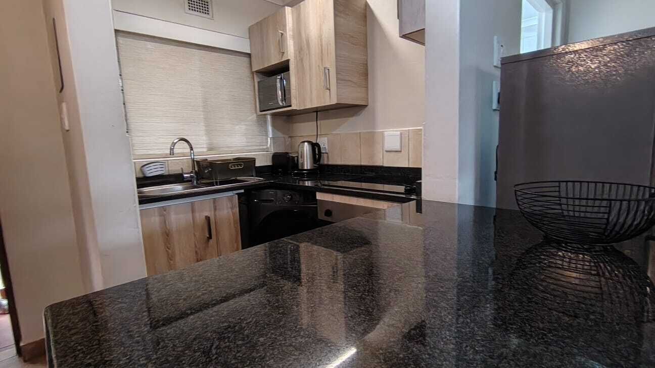 A kitchen with a granite countertop, wooden cabinets, and a stainless steel sink.