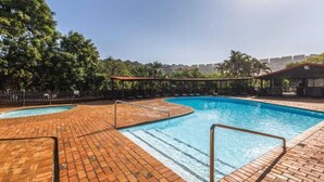 Ein Schwimmbecken mit Backstein-Terrasse, umgeben von Bäumen und einem Zaun.