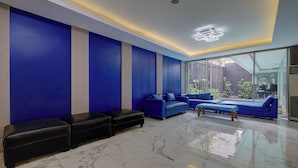 A modern living room with a blue sofa set, black ottomans, and a glass wall offering a view of the outdoors. - Hotel Bunga-Bunga By ARBA (Jakarta)
