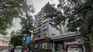 A multi-story hotel with a colorful facade, a covered entrance, and a parking area with several vehicles and motorcycles. - Hotel Bunga-Bunga By ARBA (Jakarta)