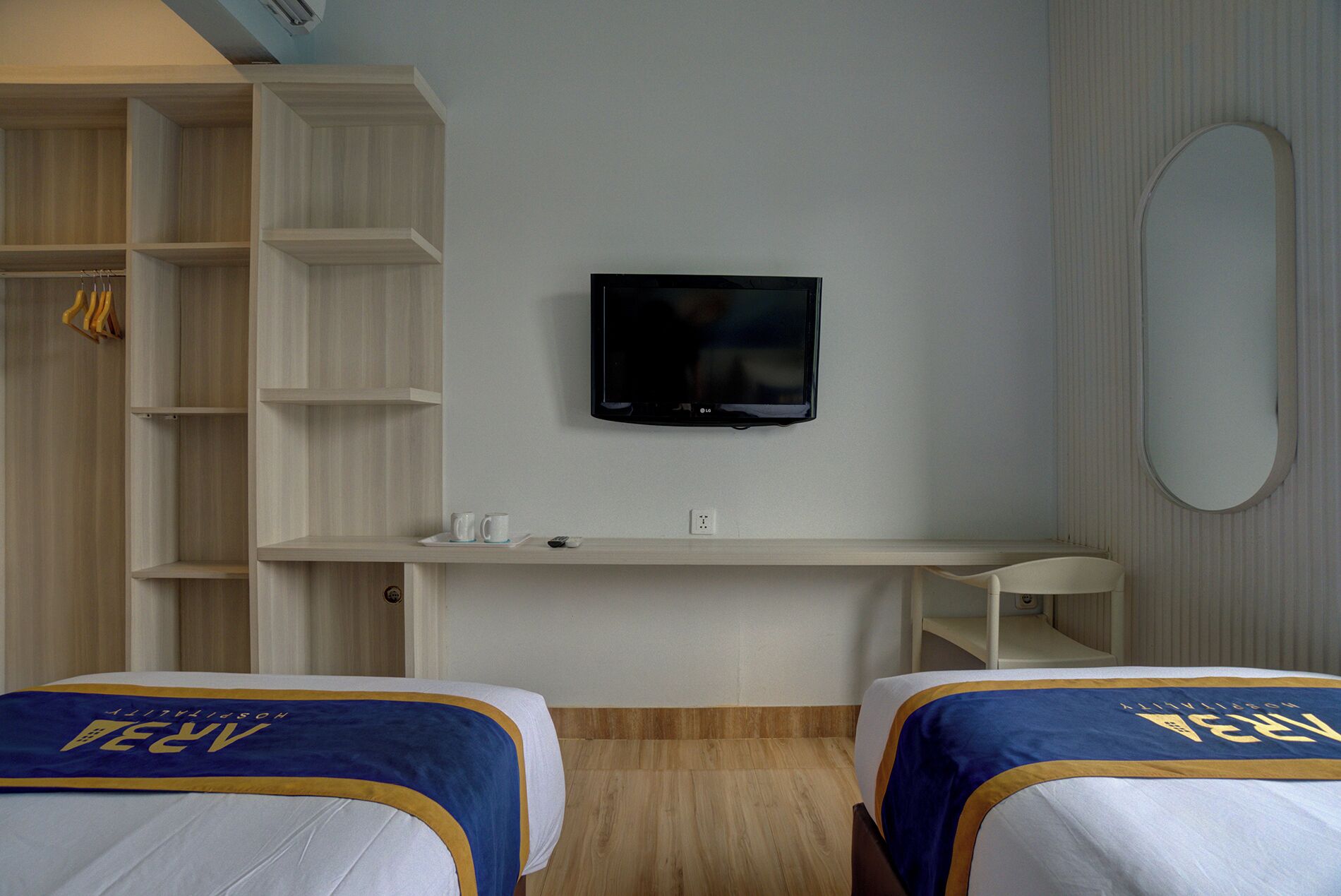 Habitación de hotel con una televisión montada en la pared, un escritorio con una silla y dos camas con cabeceros a juego.