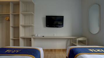 A hotel room with a TV mounted on the wall, a desk with a chair, and two beds with matching headboards.
