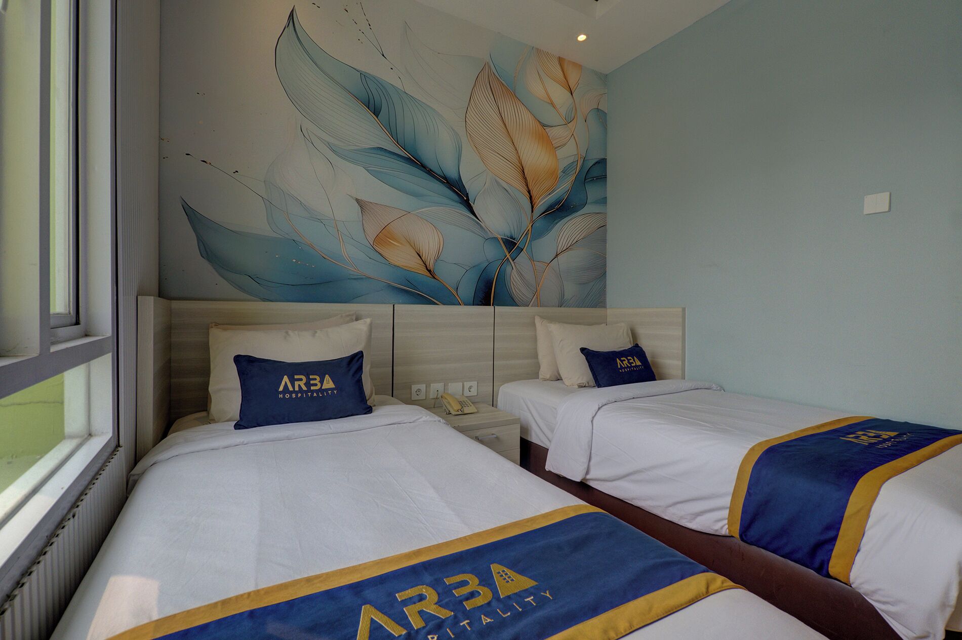 A hotel room with two beds, a large abstract mural on the wall, and a window with blinds.
