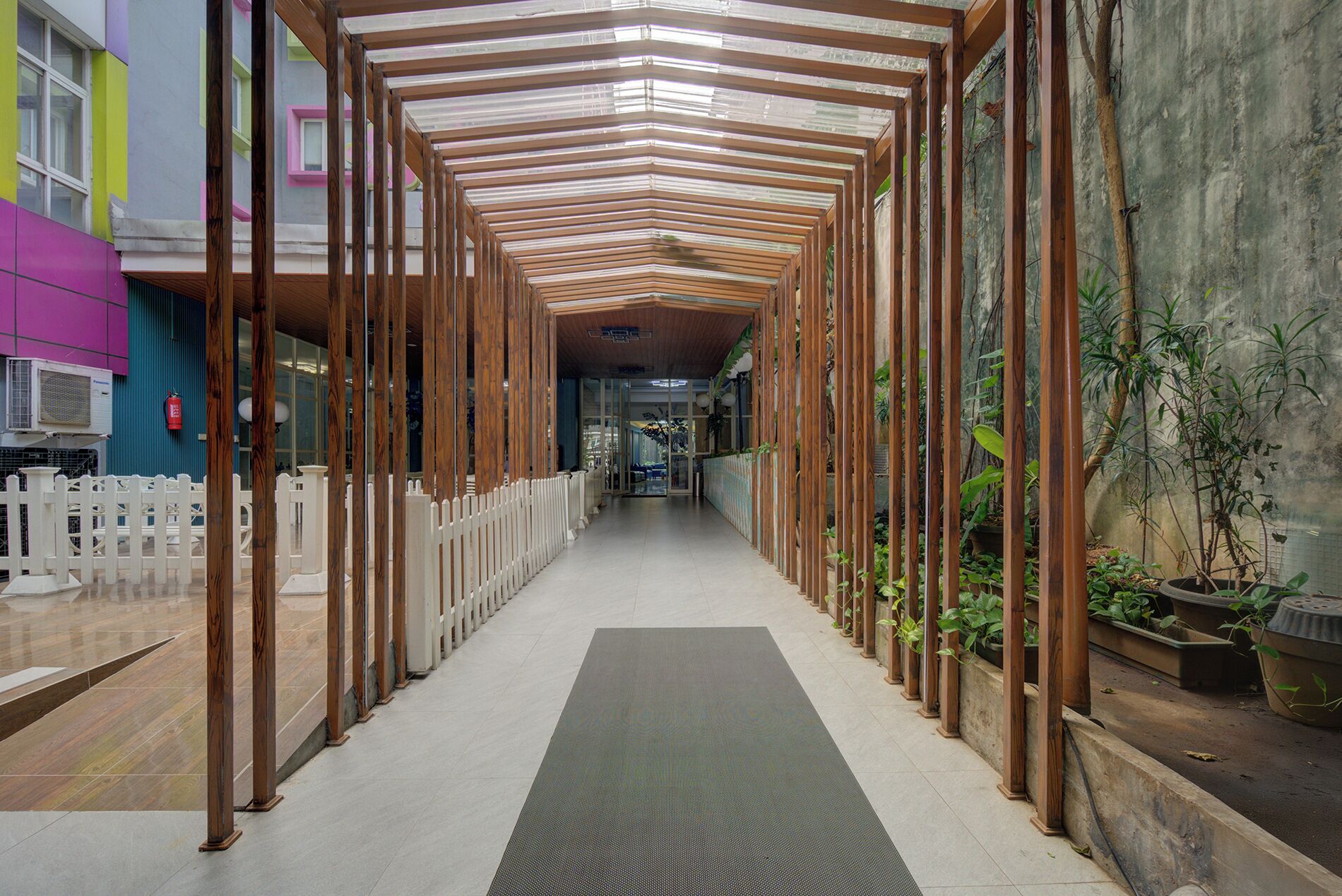 A corridor with wooden columns, a white picket fence, and potted plants.