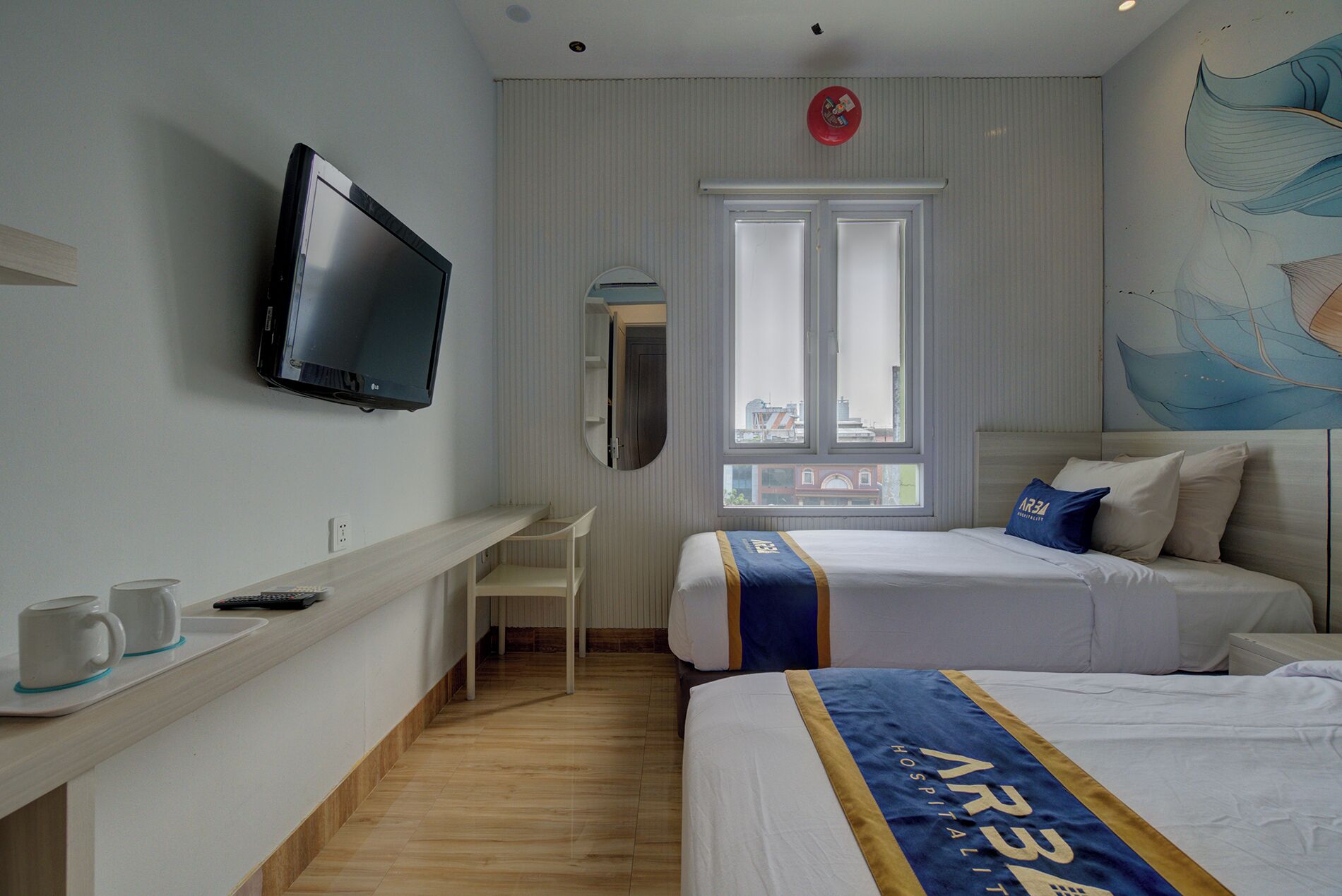 A hotel room with a bed, a desk with a computer, a television, and a window with a view of buildings.