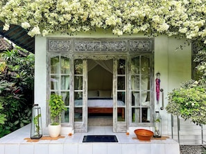Una habitación con cama, ventana con cortinas, una planta en maceta y un farol.