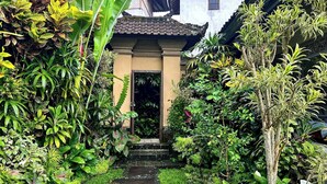 Uma trilha no jardim leva a um edifício com telhado em telhas e uma porta.