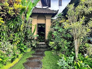Un sendero en un jardín que lleva a un edificio con techo de tejas y una puerta.
