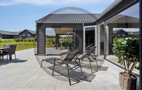 Une terrasse extérieure couverte, aménagée avec des chaises longues, une table et un pot de fleurs.