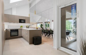 A modern kitchen with built-in appliances, a dining area with a large table, and a view through a glass door. - Amazing home in Bogense with sauna (Bogense)
